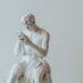 A white marble sculpture of a man sitting and looking at a smartphone.