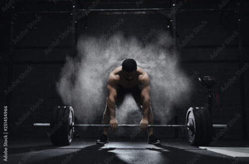 Crossfit athlete preparing to lift heavy barbell in a cloud of dust at the gym. Barbell magnesia protection.