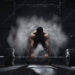 Crossfit athlete preparing to lift heavy barbell in a cloud of dust at the gym. Barbell magnesia protection.