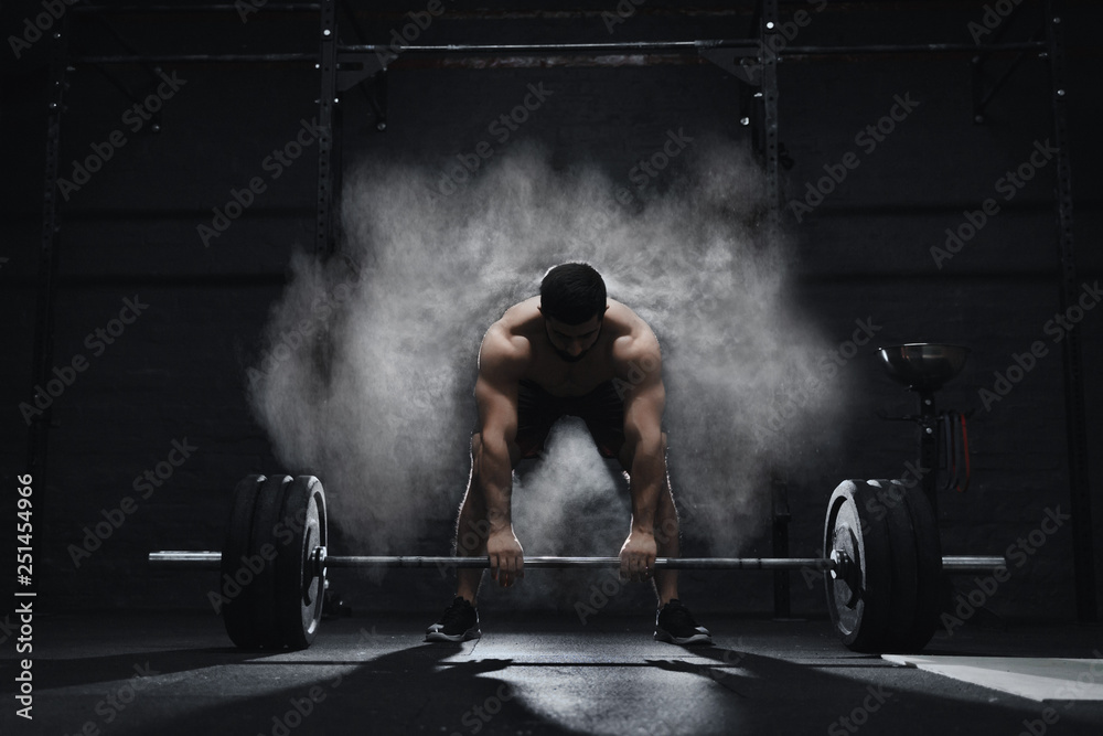 Crossfit athlete preparing to lift heavy barbell in a cloud of dust at the gym. Barbell magnesia protection.